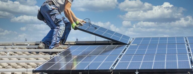 Handwerker installieren auf einem Dach Photovoltaikelemente für eine Heiz-PV Anlage.